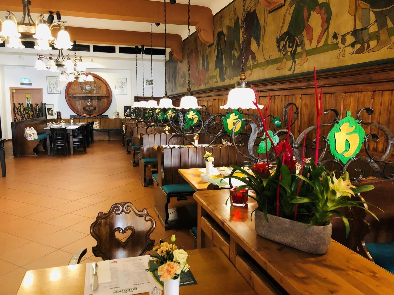 A restaurant with wooden furniture, hanging light fixtures, and a mural on the wall.