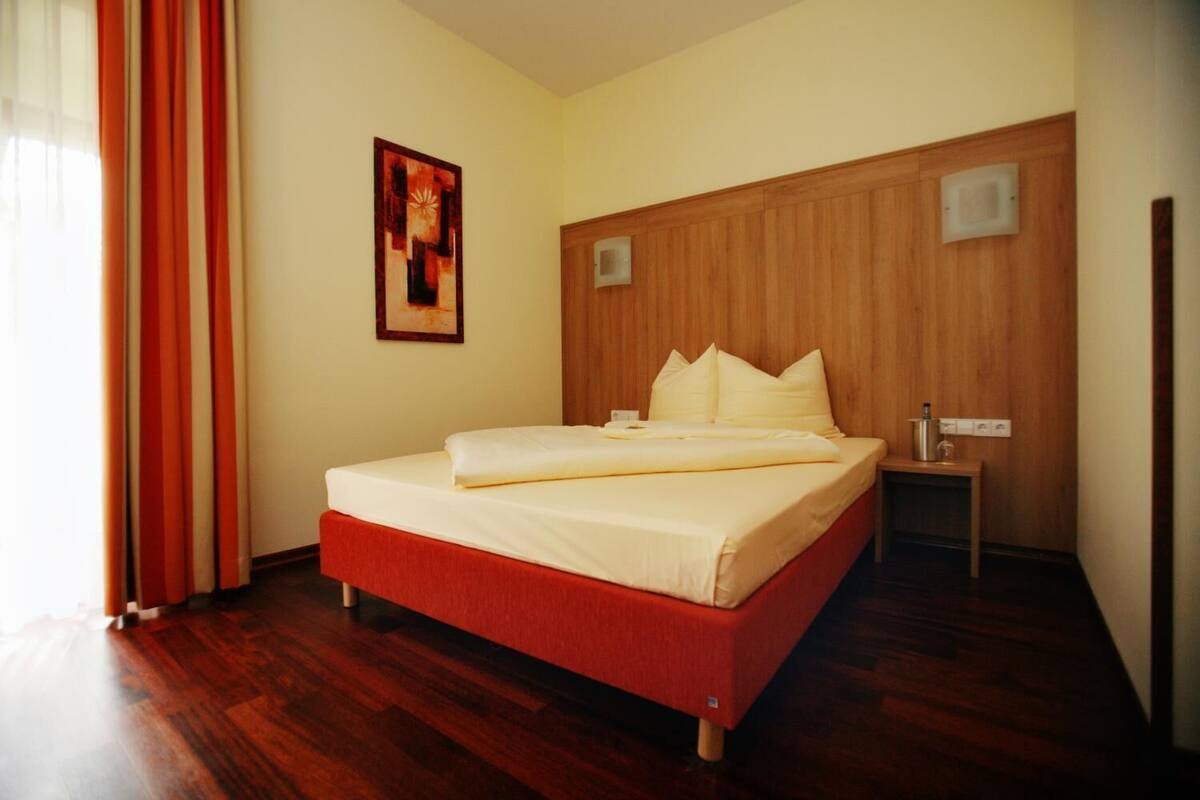Ein Hotelzimmer mit einem Holz-Kopfteil, einem Bett mit weißer Bettwäsche, einem Nachttisch und einer Wandleuchte.
