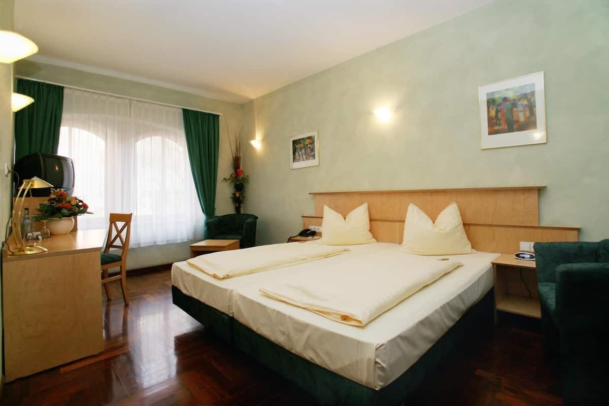 Ein Hotelzimmer mit einem großen Bett, einem Schreibtisch mit Lampe, einem Sessel und einem Fernseher.