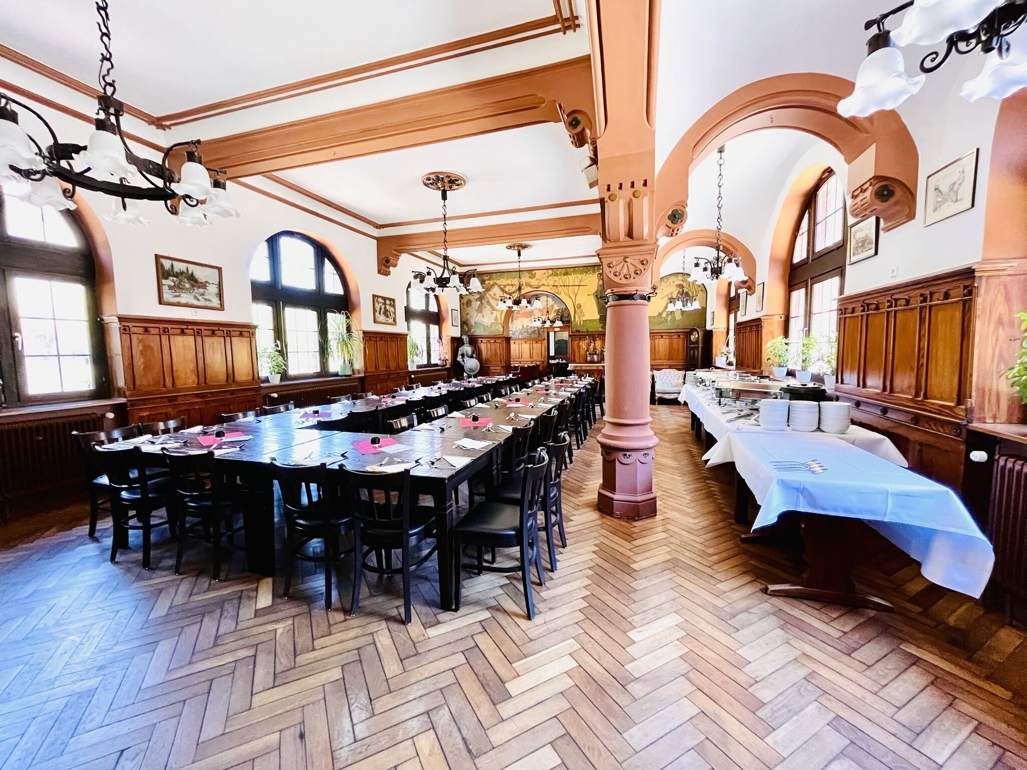 Ein großer Festsaal mit langen Tischen, Holzvertäfelung und Kristalllüstern.