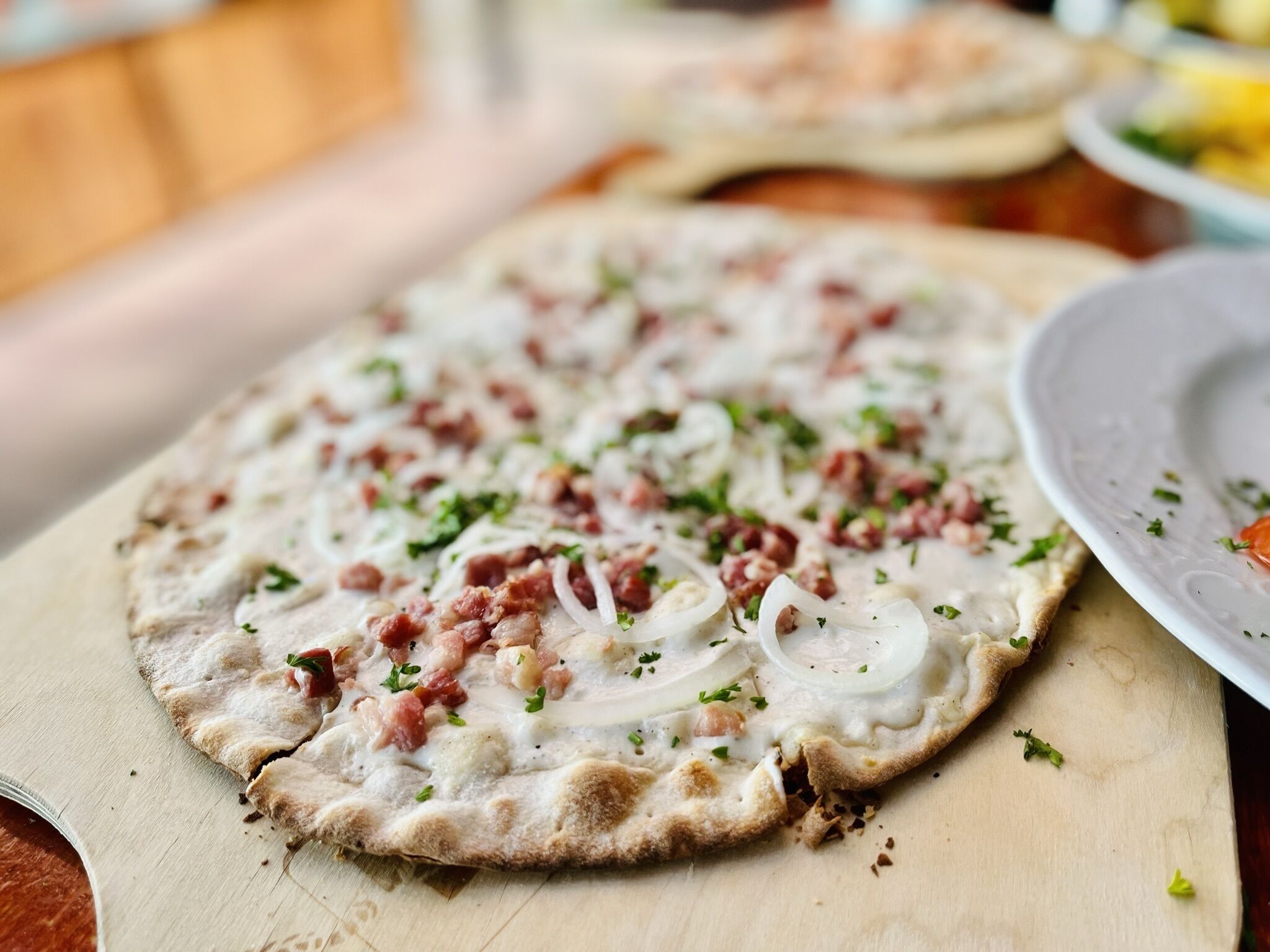 Une pizza sur une planche en bois, garnie de divers ingrédients, et une assiette à proximité.