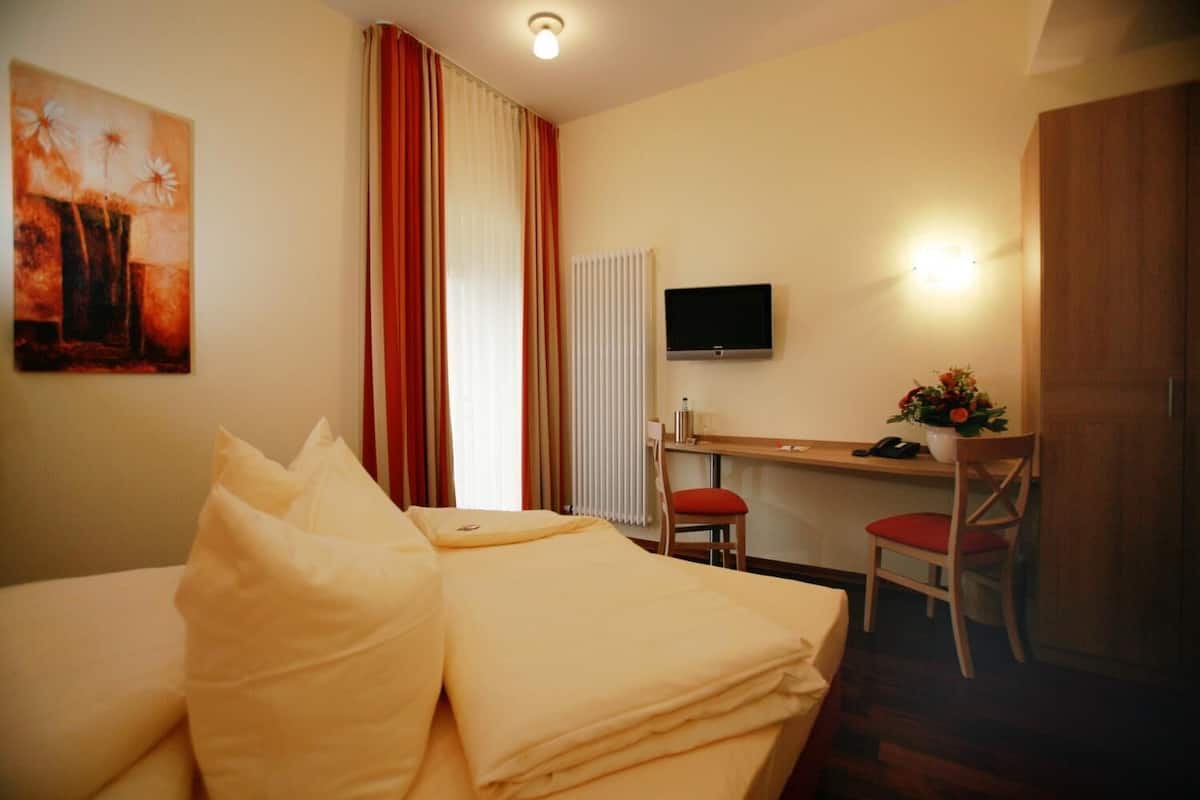 Ein Hotelzimmer mit Bett, Schreibtisch, Stuhl, Fernseher und einem Bild an der Wand.