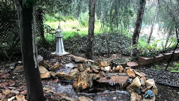 Ein Garten mit einem kleinen Wasserfall, umgeben von Steinen und Bäumen.