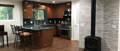 A modern kitchen with wooden cabinets, a central island, a stove, and a black wood-burning stove.