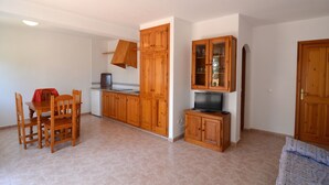 Una cocina compacta con armarios de madera, una mesa de comedor con sillas y un televisor.