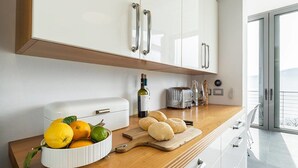 A modern kitchen with white cabinets, a wooden countertop, a fruit bowl, a bottle of wine, a toaster, and a cutting board with bread. - Luxury Italian Lakes Villa With Private Pool, Gym, Bbq, Wifi, Lake Views (Verbania)