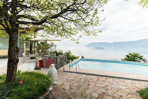 A pool area with a stone pathway, a statue, and a view of a body of water with distant land.