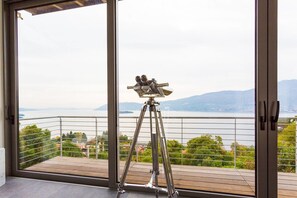 A telescope on a balcony overlooking a lake with mountains in the distance.