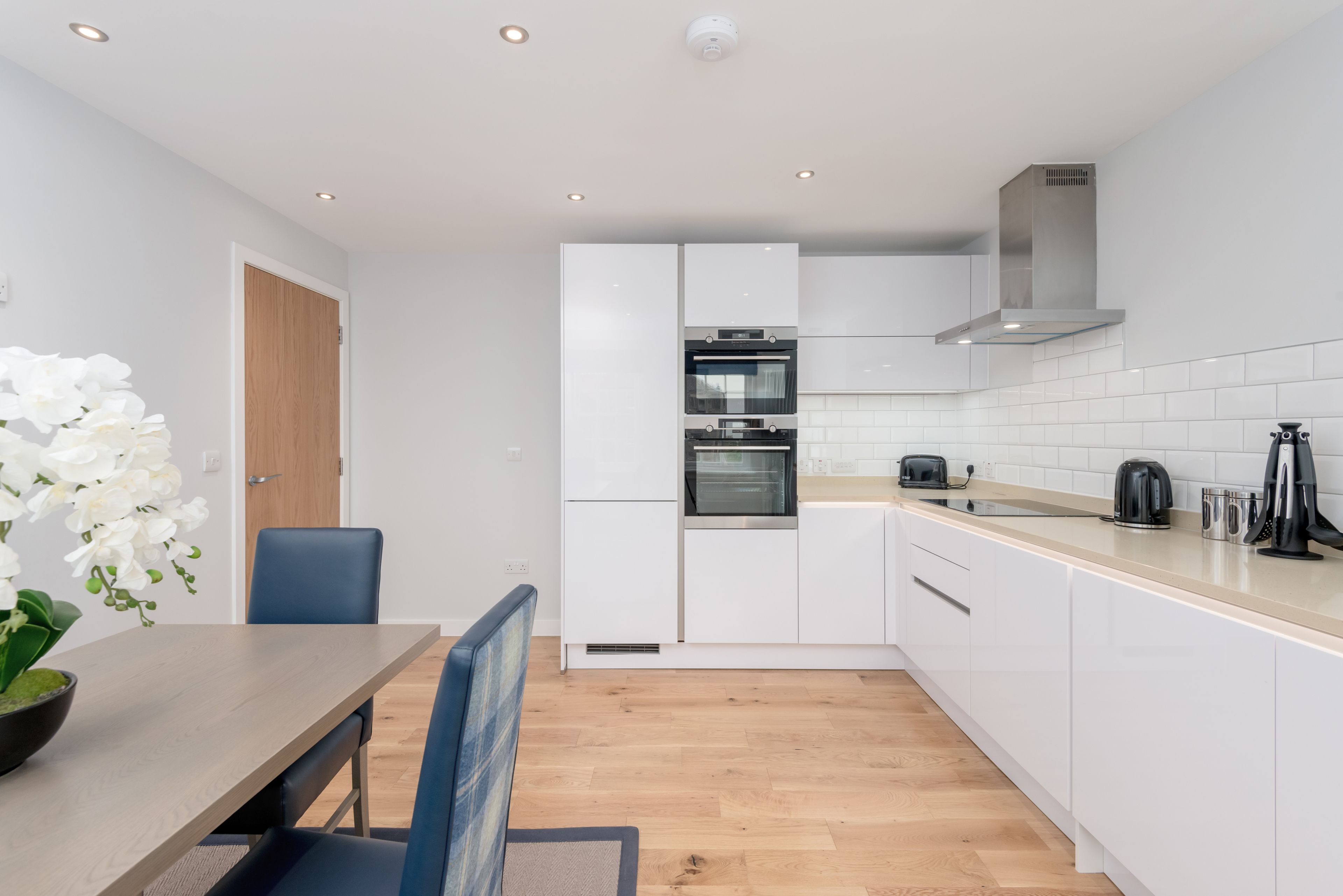 Una cocina moderna con armarios blancos, una mesa de comedor de madera y una silla azul.
