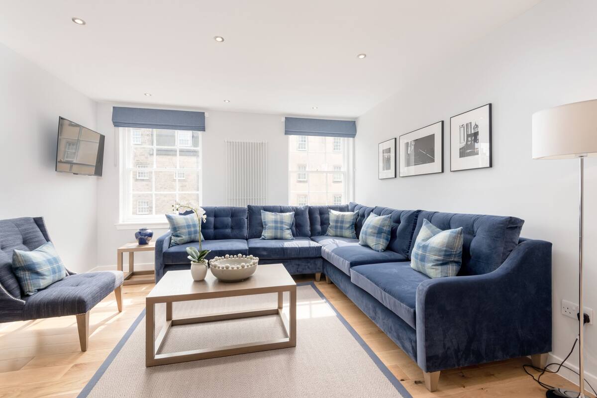 A modern living room with a blue sectional sofa, a wooden coffee table, and a potted plant.