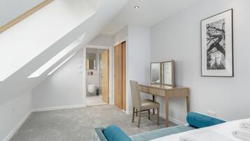 A modern bedroom with a skylight, a desk with a chair, a bed with blue and white bedding, and a framed picture on the wall.