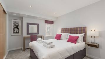 A modern bedroom with a large bed, a bedside table with a lamp, a window with a view, and a framed picture on the wall.