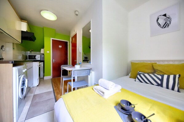 A compact hotel room with a bed, a small kitchenette, a dining area, and a bathroom.