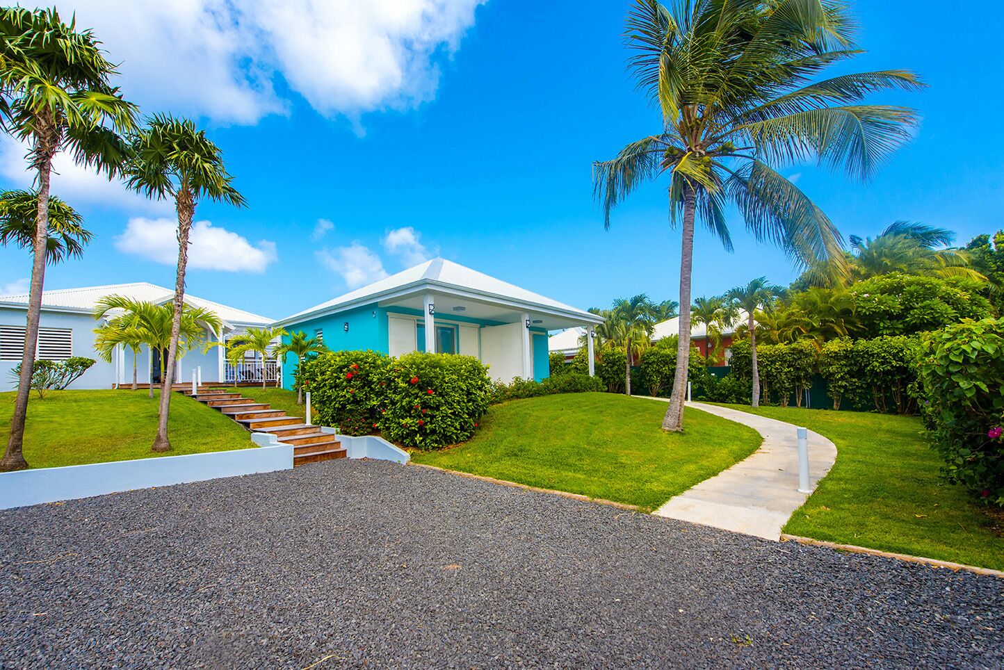 A modern two-story house with a blue exterior, surrounded by a well-maintained lawn and palm trees.