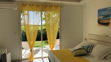 A bedroom with a bed, yellow curtains, a ceiling fan, and a view of a garden.