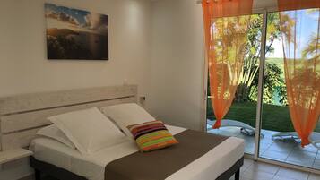 A bedroom with a bed, a nightstand, a painting, and a view of a garden through a glass door.