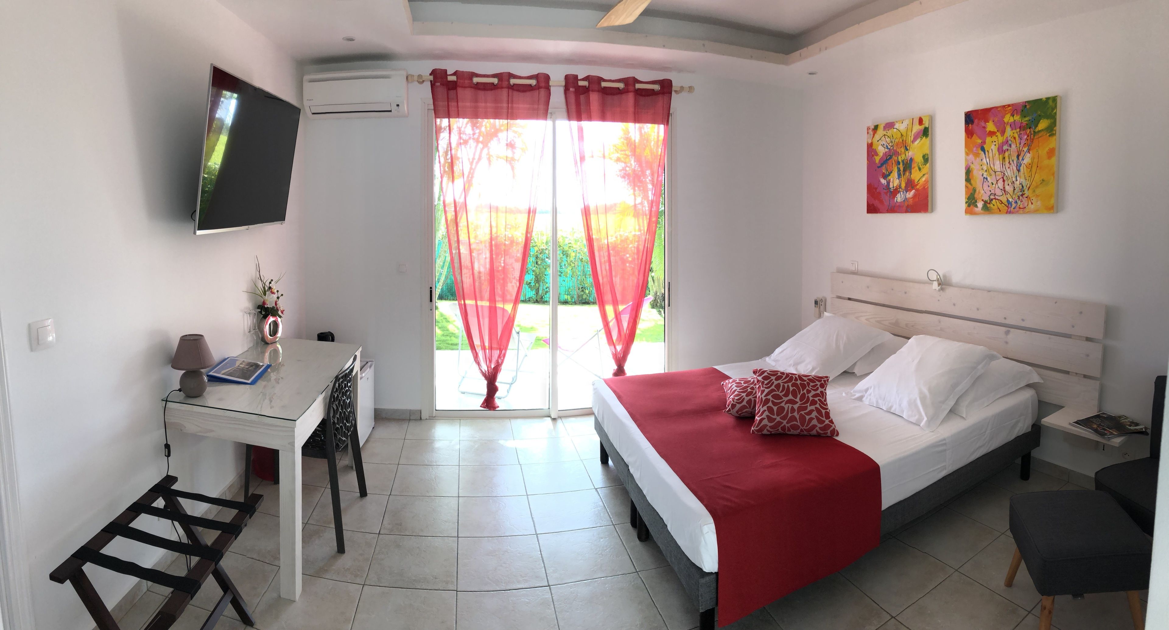 Ein Schlafzimmer mit einem Bett, einem Schreibtisch, einem Sessel, einem Fernseher und einem Fenster mit Vorhängen.