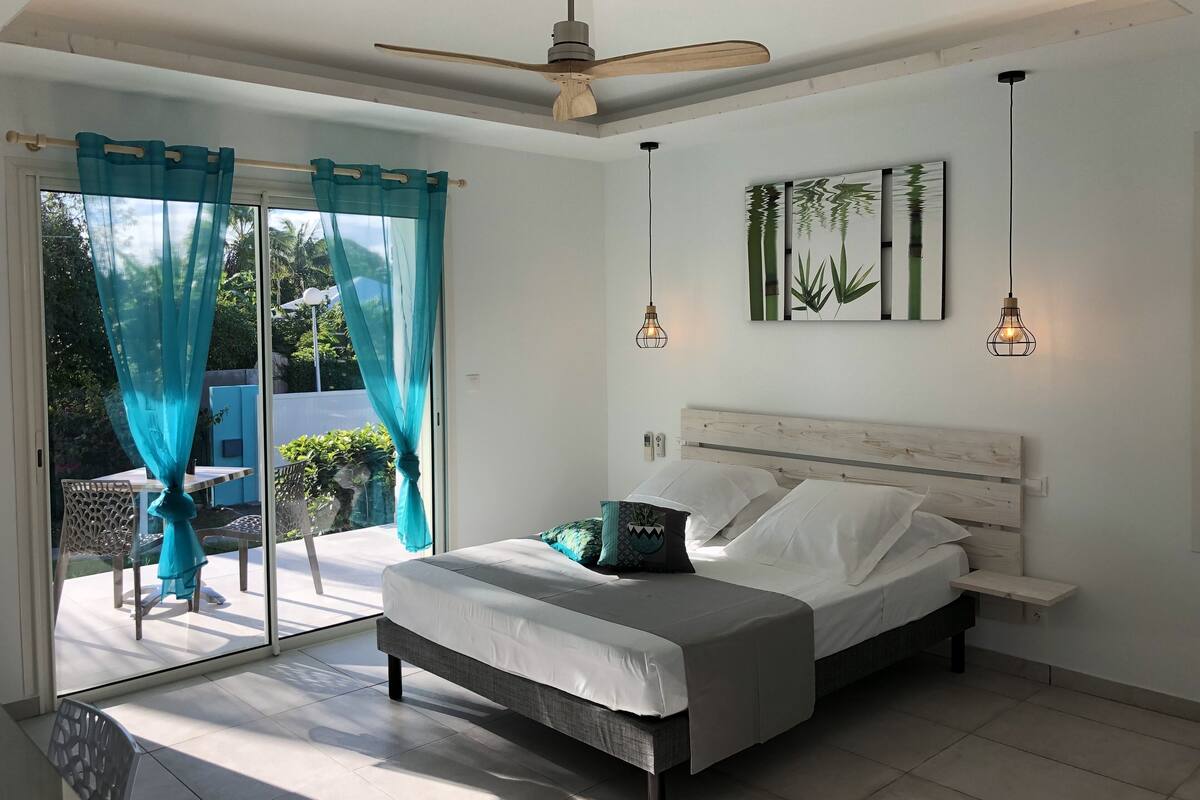 A bedroom with a bed, a ceiling fan, a wall-mounted light fixture, and a sliding glass door leading to an outdoor area.