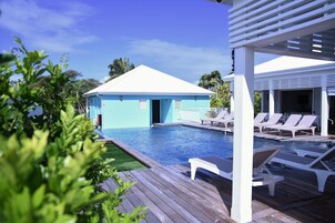 Uma área de piscina com um prédio azul claro, cadeiras de lounge brancas e um deck de madeira.