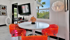 Une pièce moderne avec une table ronde, deux chaises orange, un globe en guise de décoration centrale, un téléviseur fixé au mur et une fenêtre donnant sur un paysage verdoyant.