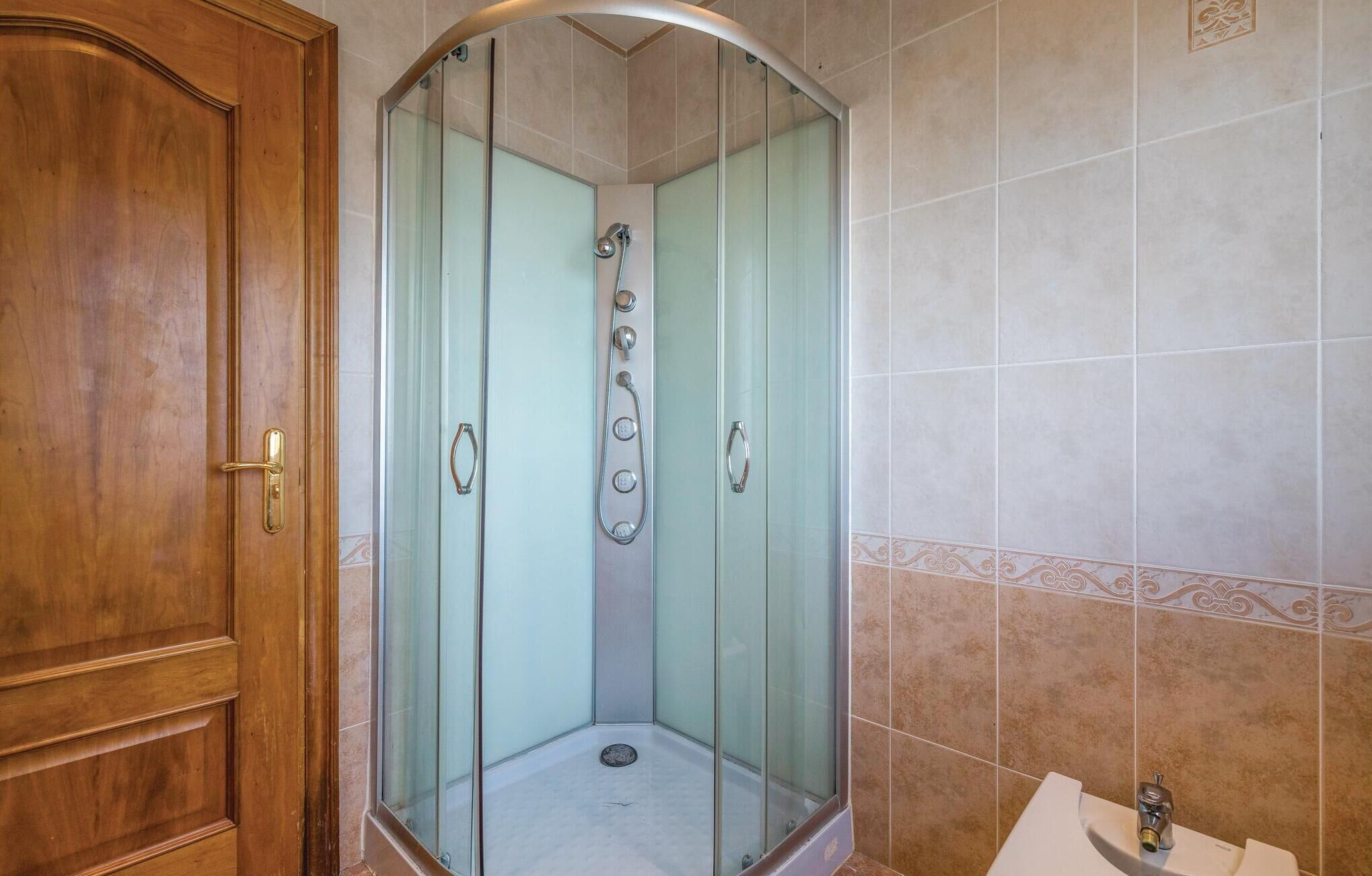 A shower with a glass door, a wooden door to the left, and a tiled wall with a decorative border.