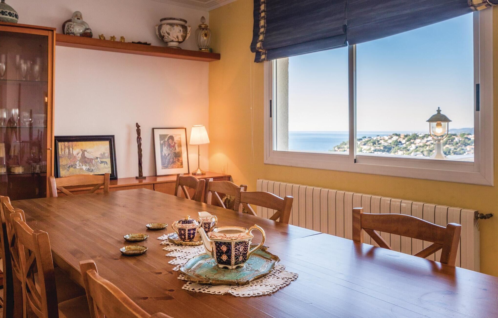 Een eethoek met een houten tafel gedekt voor vier personen, uitzicht op zee door een groot raam en een radiator aan de muur.