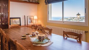 Un coin repas avec une table en bois dressée pour quatre personnes, une vue sur la mer par une grande fenêtre et un radiateur au mur.