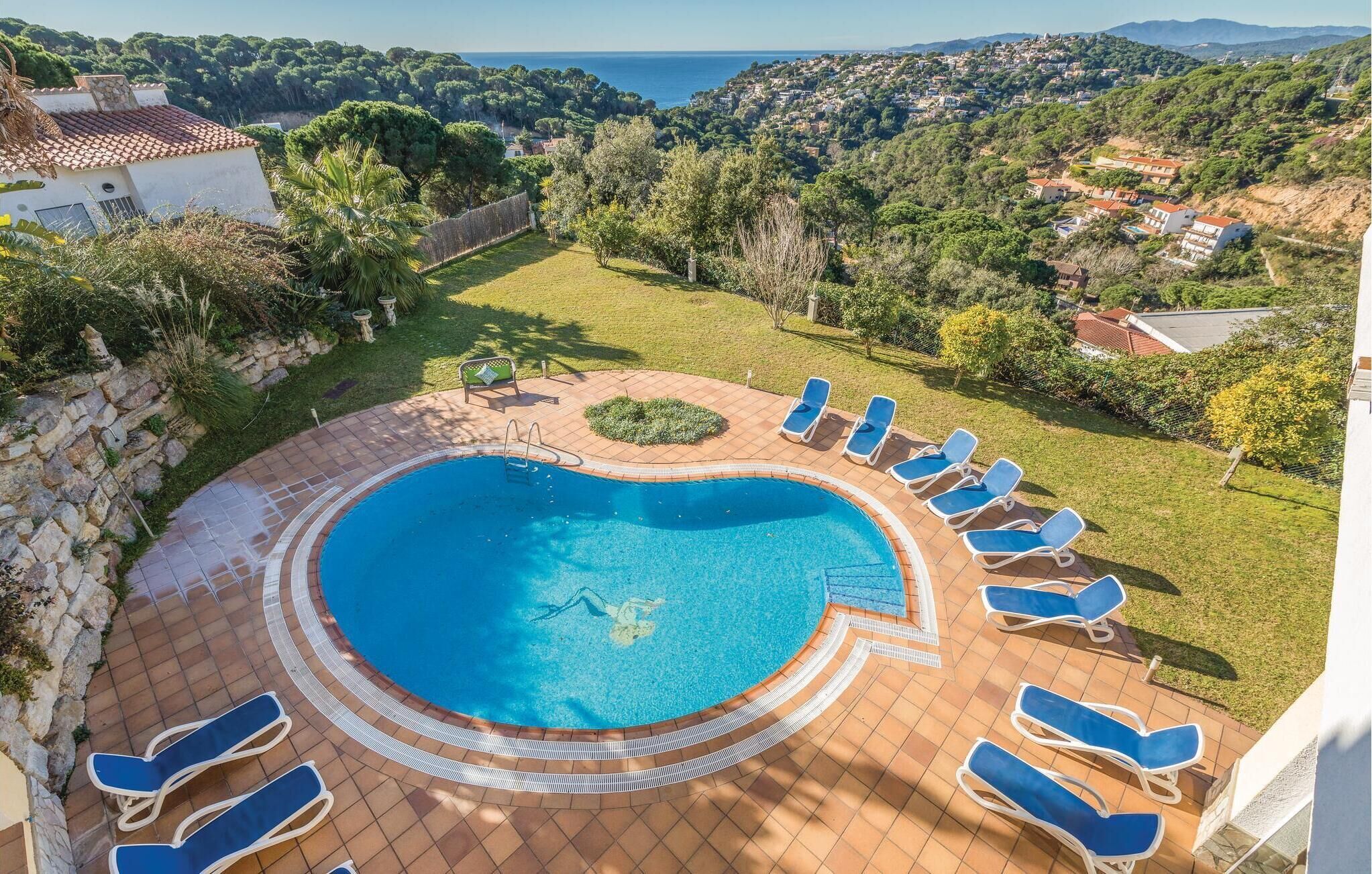 Een rond zwembad met een omliggend terras, ligbedden en uitzicht op een kustlandschap.