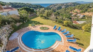 Une piscine ronde entourée d’une terrasse, de chaises longues et offrant une vue sur un paysage côtier.