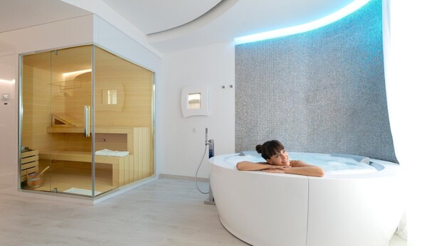 A modern spa room with a large, curved hot tub, a glass-enclosed sauna, and a minimalist design. - AHD Rooms (Milan)