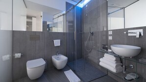 A modern bathroom with a glass shower enclosure, a bidet, a large sink, and a glass-topped vanity. - AHD Rooms (Milan)