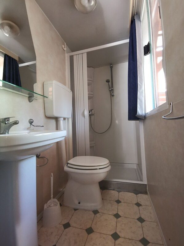 A bathroom with a toilet, sink, shower, and a glass shelf. - Baia Calenella (Vico del Gargano)