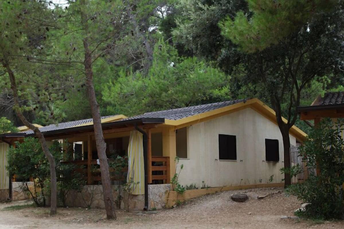 A rustic cabin with a tiled roof, a wooden porch, and a stone foundation.