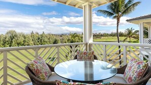 A covered outdoor seating area with a round glass table and wicker chairs, overlooking a well-maintained lawn and distant mountains.