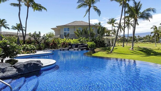 A swimming pool with a house in the background, surrounded by palm trees and greenery.