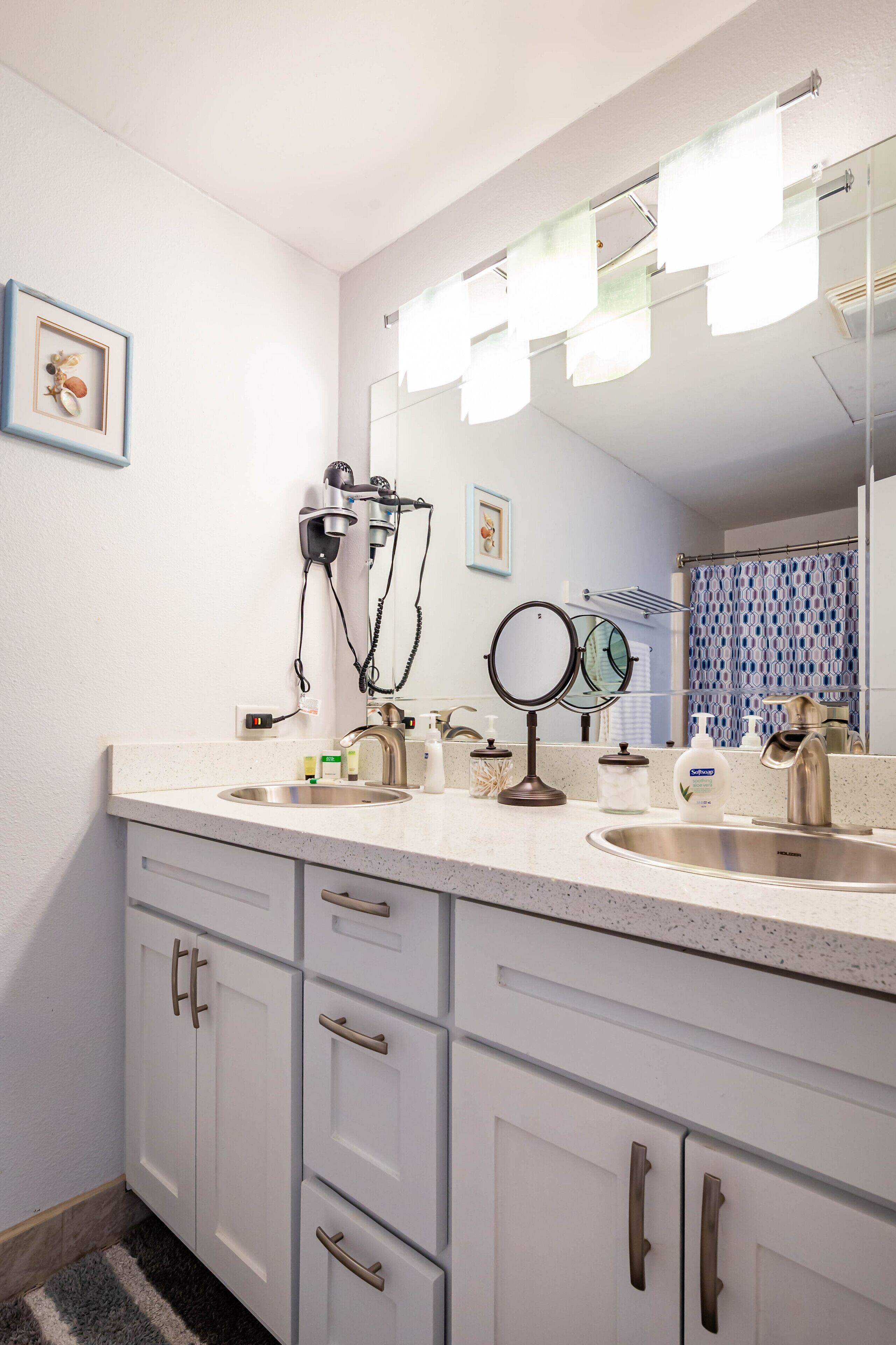 A bathroom with a double sink, a hairdryer, a mirror, and a shower curtain.