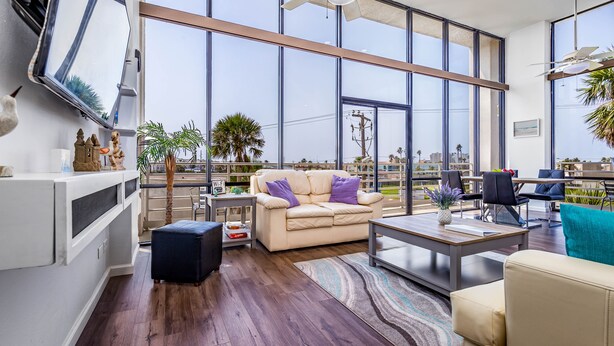 A spacious living room with a large window, a ceiling fan, and a view of the cityscape.