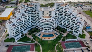 A modern multi-story hotel with a central courtyard, tennis courts, and a pool.