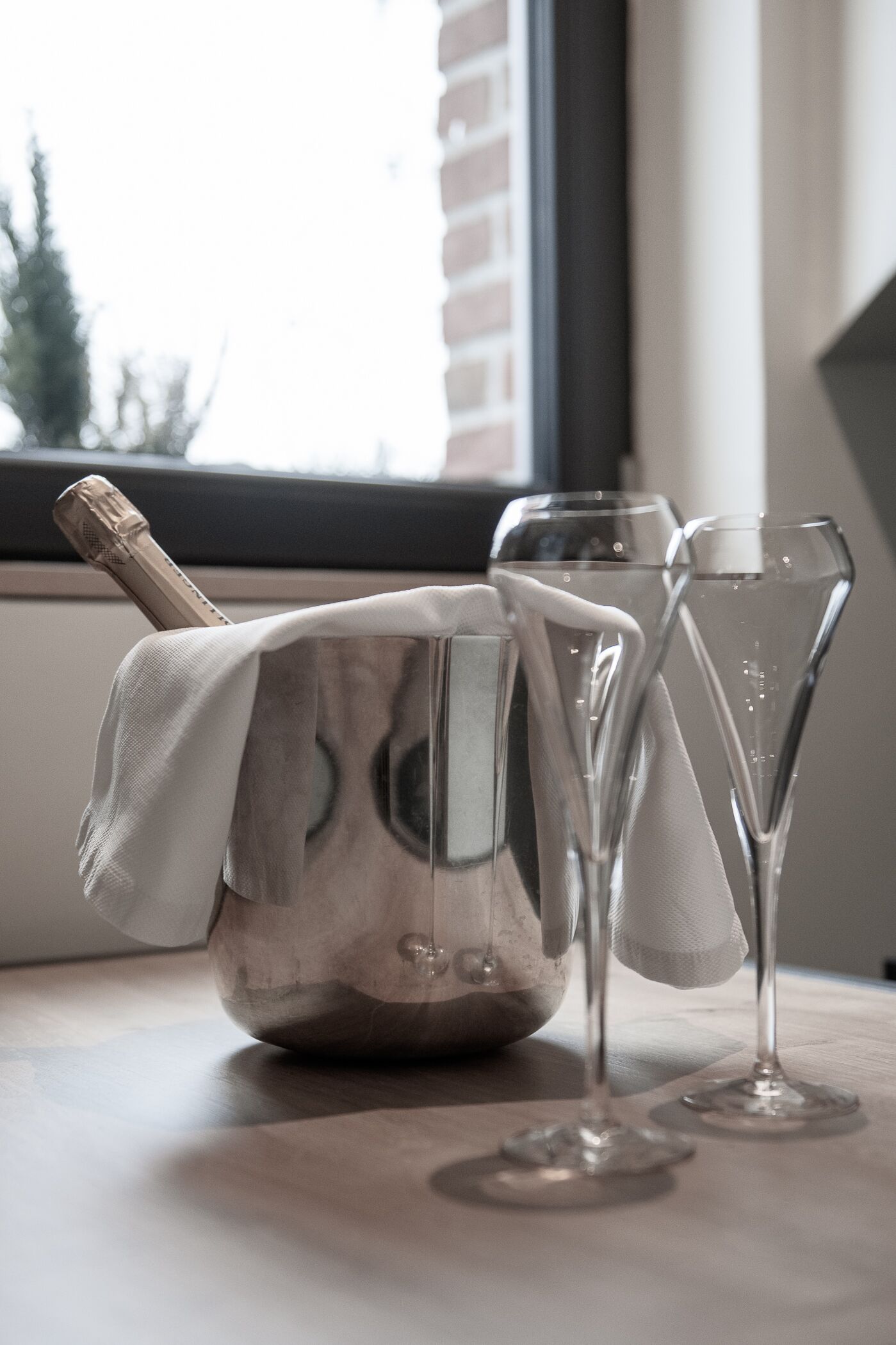 Un recipiente metálico con cubierta de tela, dos vasos de vidrio transparente y una ventana al fondo.