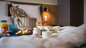 Een keurig opgemaakte ontbijtbuffet op een bed, met een rieten mand, croissants en diverse ontbijtartikelen.