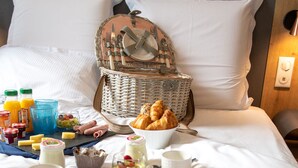 Un desayuno ordenado sobre la cama, con una cesta de mimbre, croissants y diversas delicias para el desayuno.
