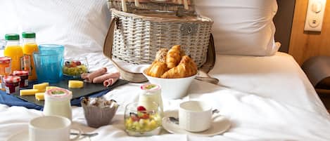 A neatly arranged breakfast setup on a bed with a wicker basket, croissants, and various breakfast items.