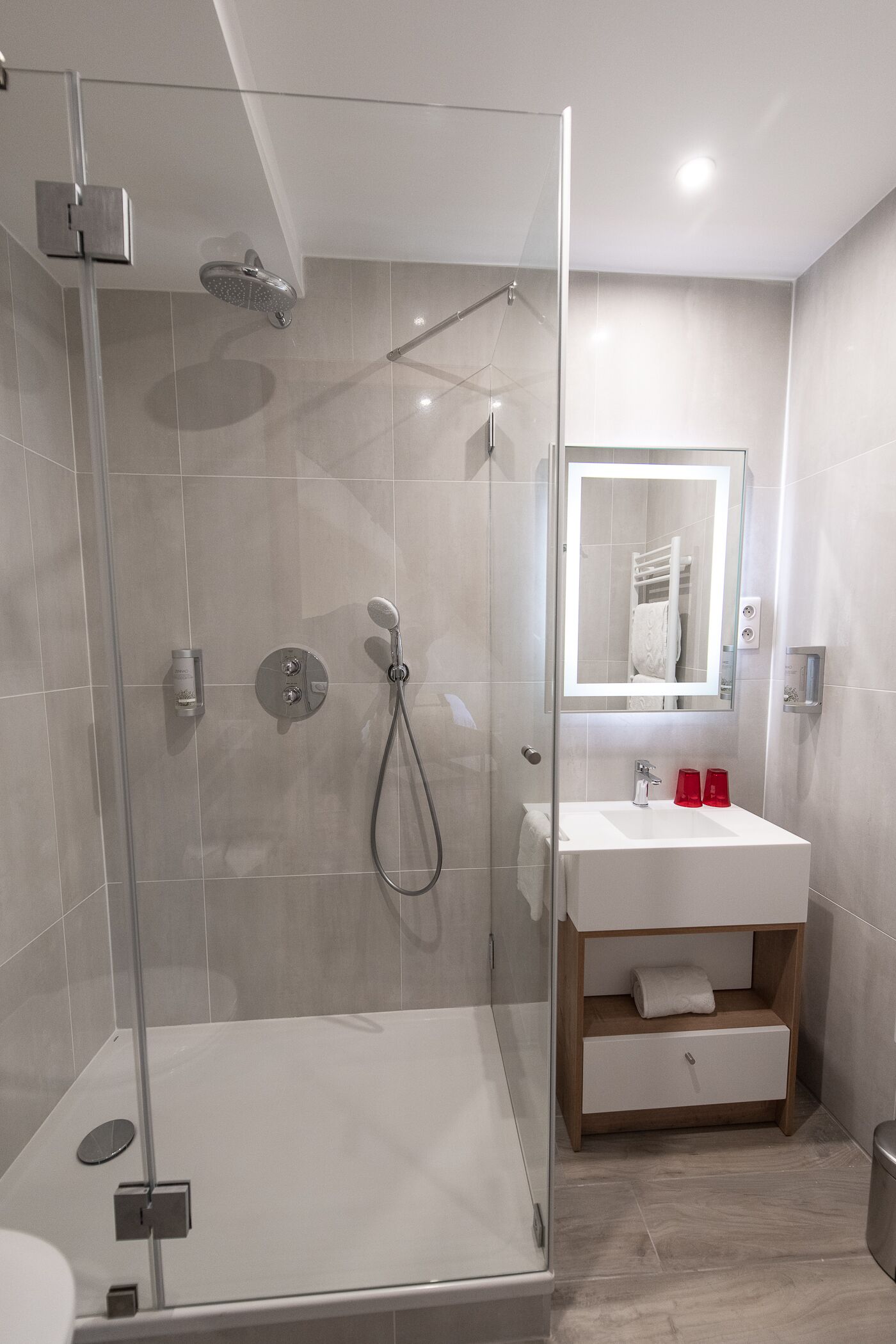 Une salle de bain moderne avec une douche à parois de verre, un lavabo blanc avec un miroir et une étagère en bois.