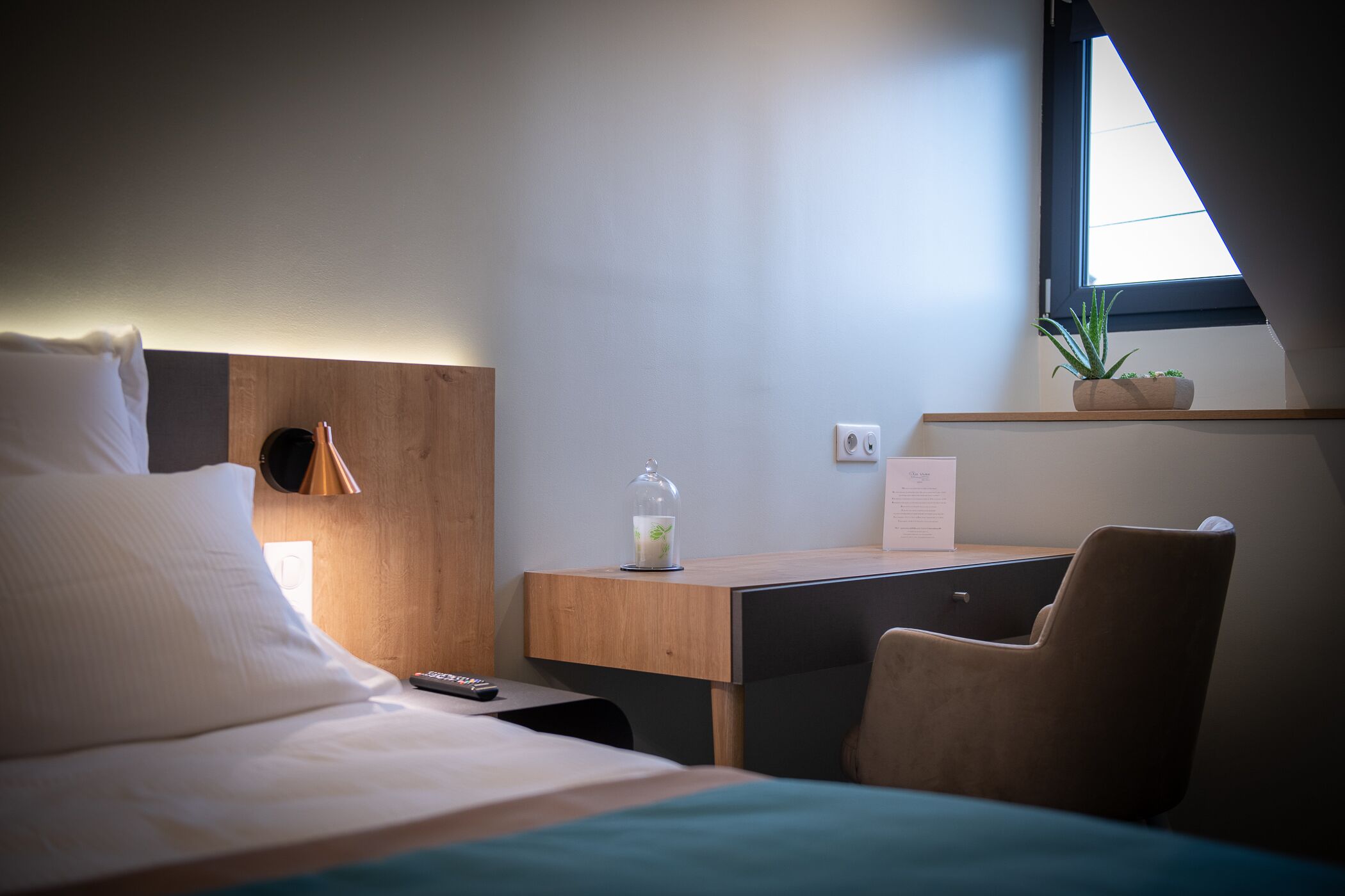Een hotelkamer met een bed, een bureau, een stoel, een bloempot en een raam.