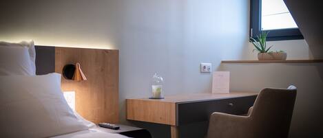 Een hotelkamer met een bed, een bureau, een stoel, een bloempot en een raam.