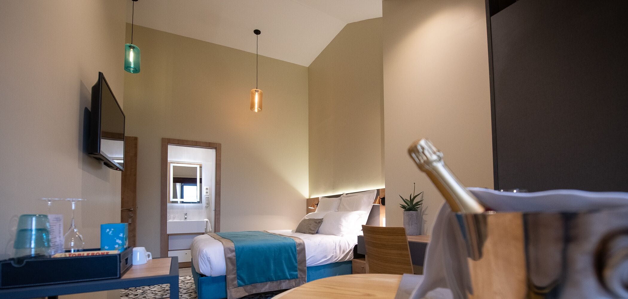 Een hotelkamer met een bed, nachtkastje, spiegel, hanglamp en een kleine potplant.