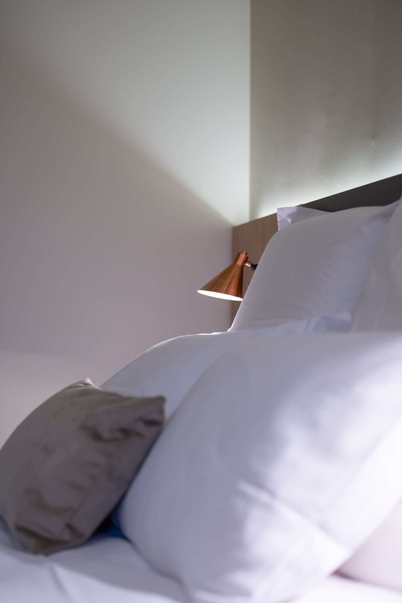Un lit bien fait, avec du linge de lit blanc et un seul oreiller gris.