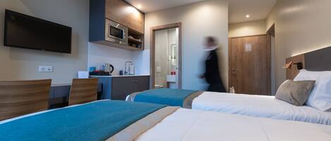 A hotel room with two beds, a desk, a microwave, and a TV.