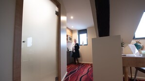 Pasillo de hotel con alfombra roja, una puerta de madera y una cocina al fondo.