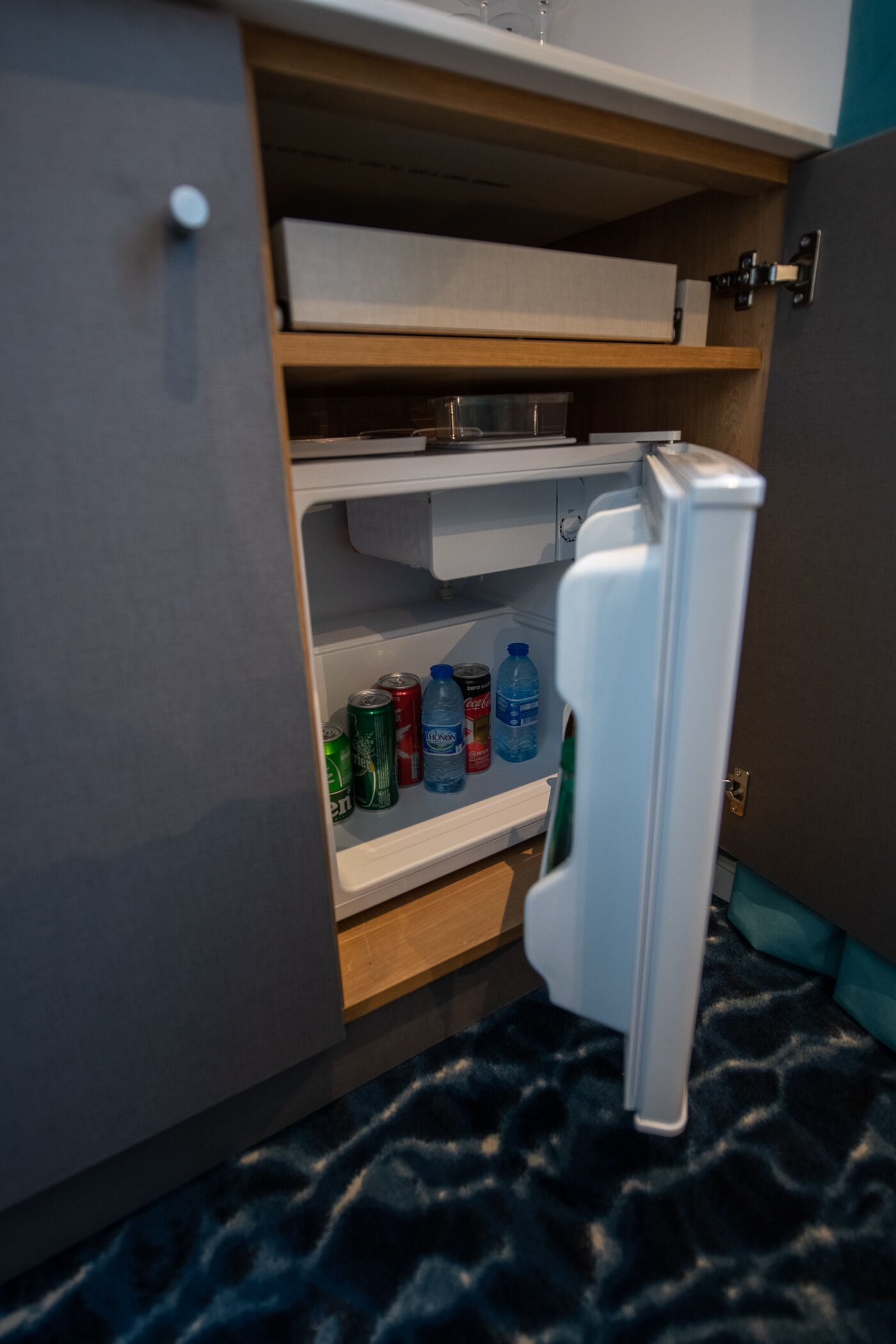 Een koelkast met planken vol drankjes en een klein vakje met een fles.